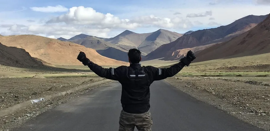 Naveen standing on a mountain road with the full mountain range visible