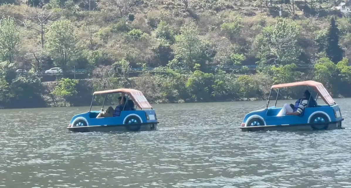 Two vehicle-shaped pedal boats moving across Bhimtal Lake