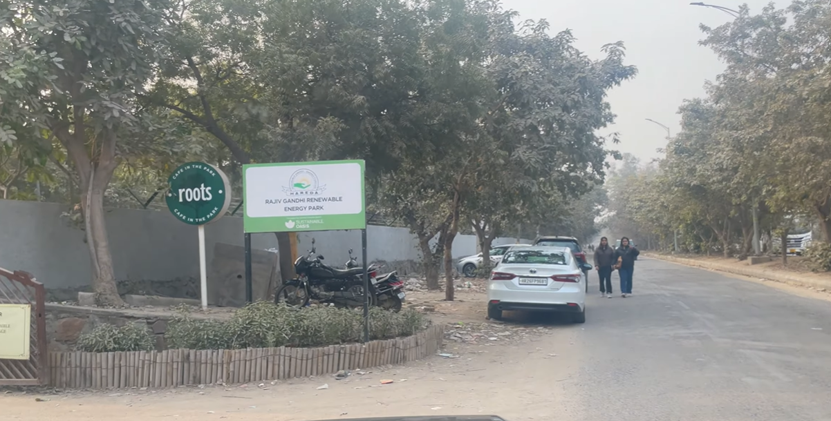 Road outside Roots Cafe Gurgaon with park sign and cars parked near the entrance