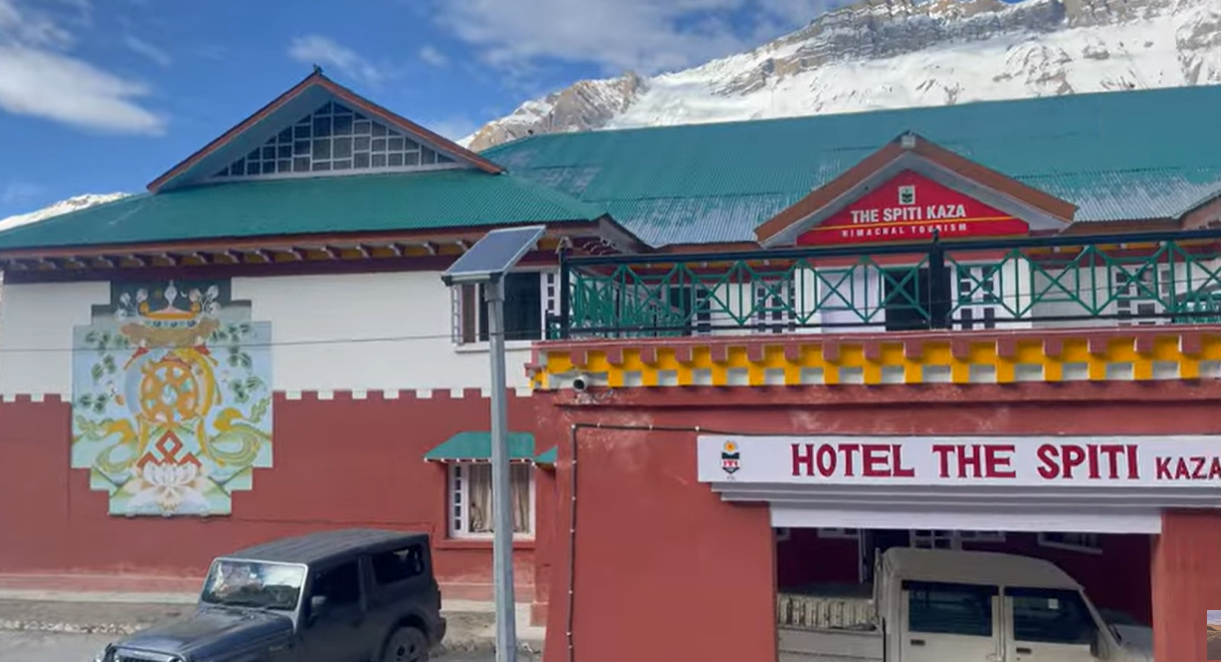 Entrance of Hotel The Spiti Kaza with vehicles and snowy mountains behind the building