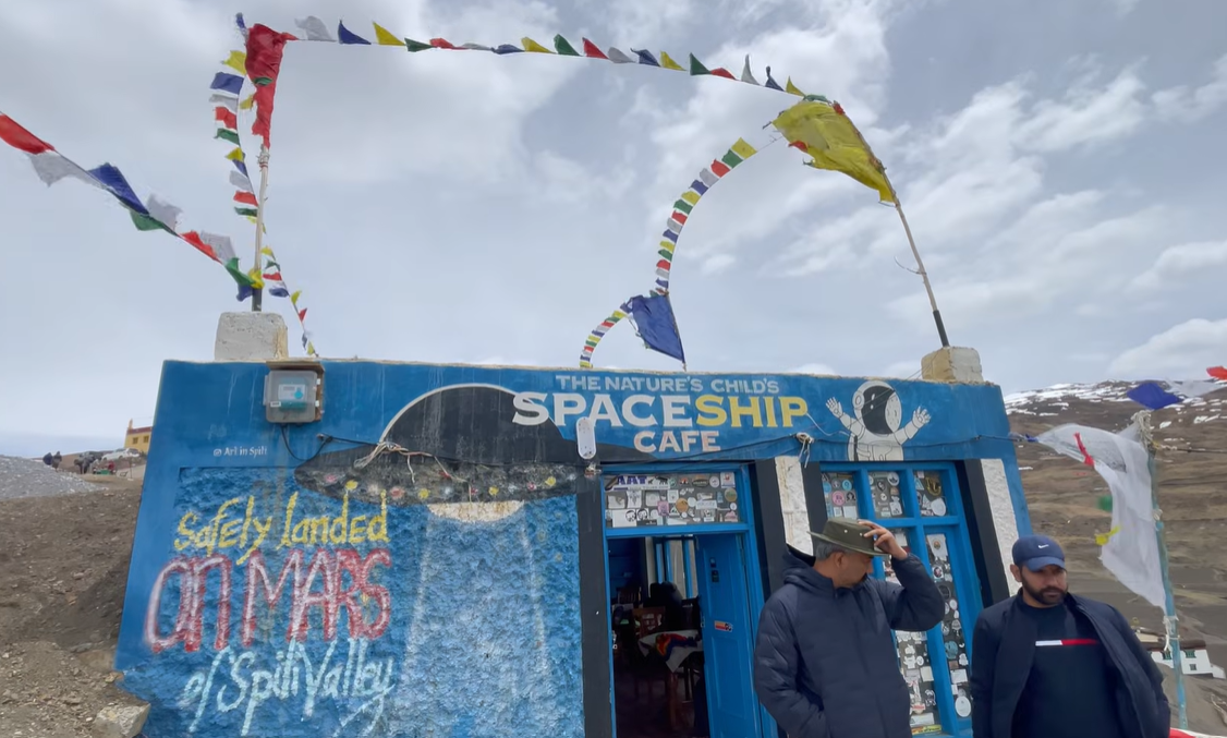 Blue exterior of The Nature's Child Spaceship Cafe in Langza with prayer flags