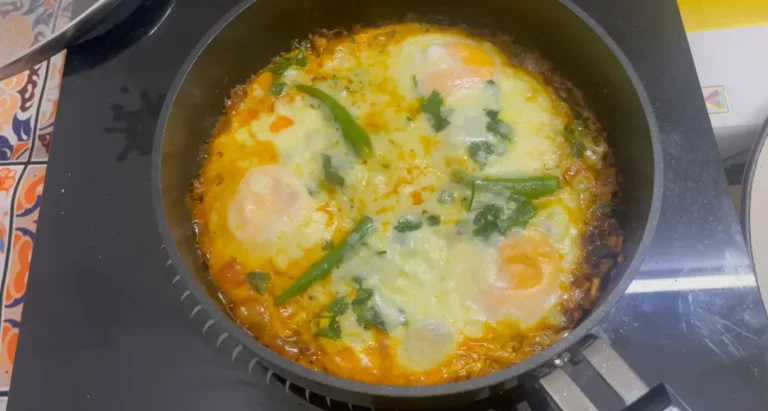 Finished egg shakshuka with melted cheese, coriander and green chillies in a black pan