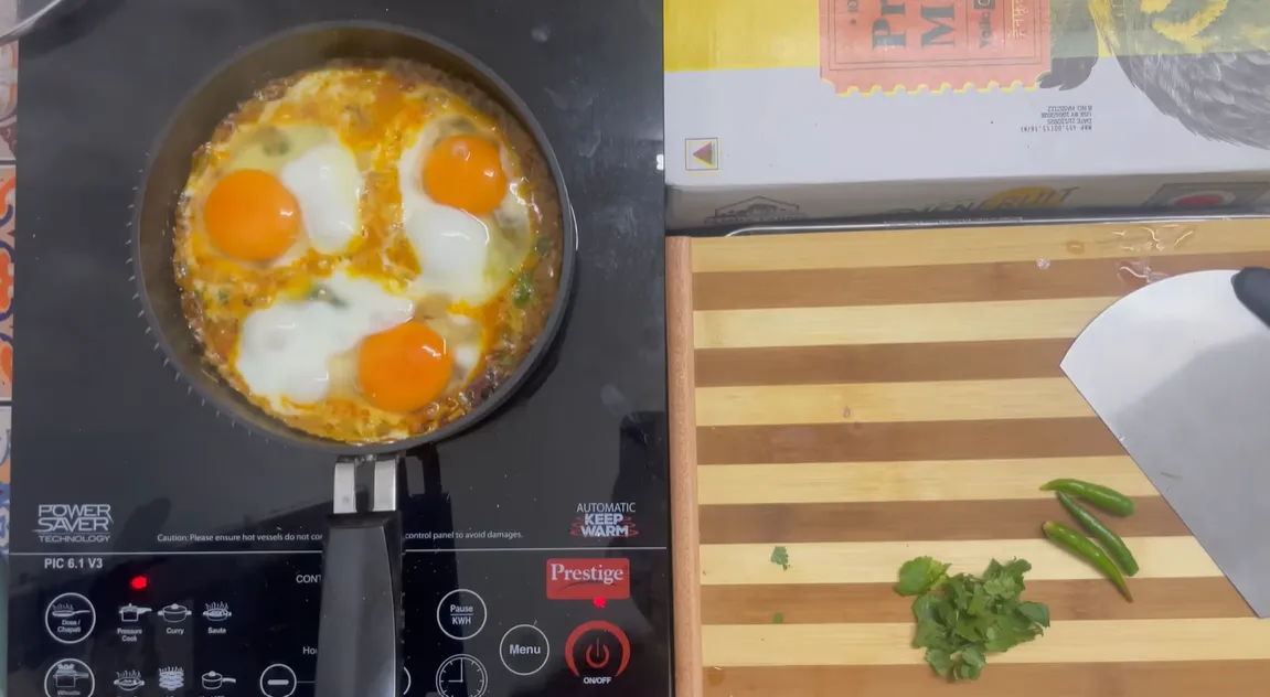 Three eggs cooking in an onion and tomato shakshuka base on an induction cooktop