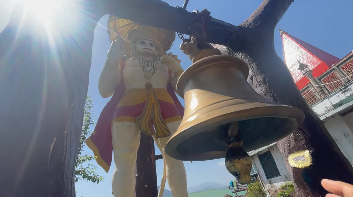 Large temple bell beside a Hanuman statue near Bhimtal