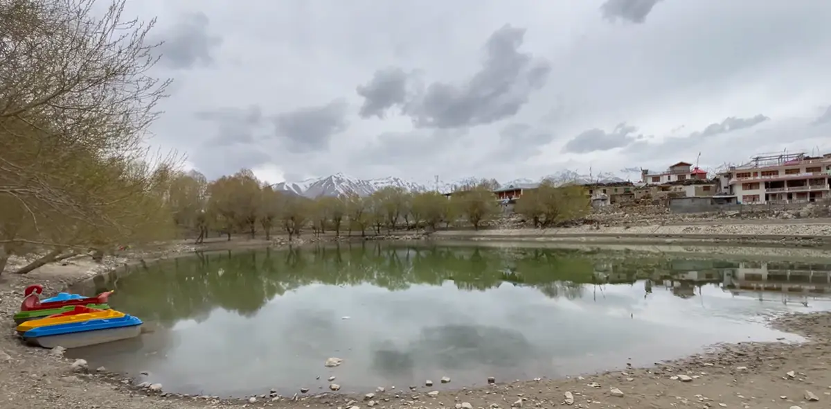 Wide view of Nako Lake with paddle boats, village houses and snowy mountains