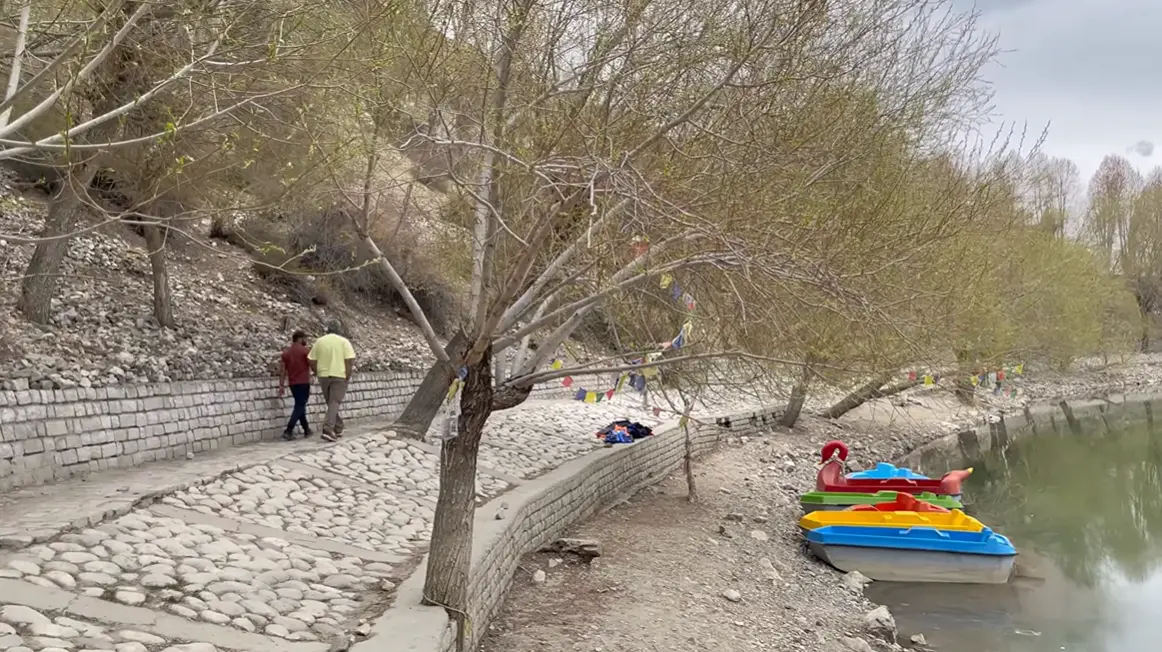 Stone walking path beside Nako Lake with prayer flags and parked paddle boats