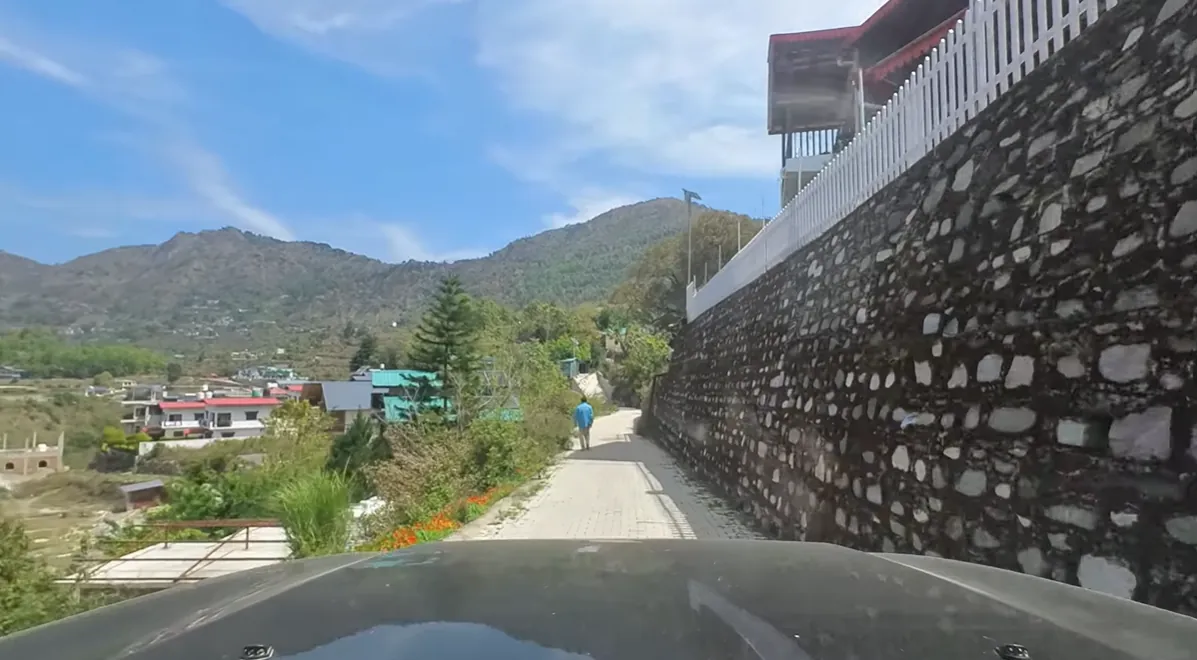 Car approaching a narrow hill road beside a stone retaining wall near Naukuchiatal