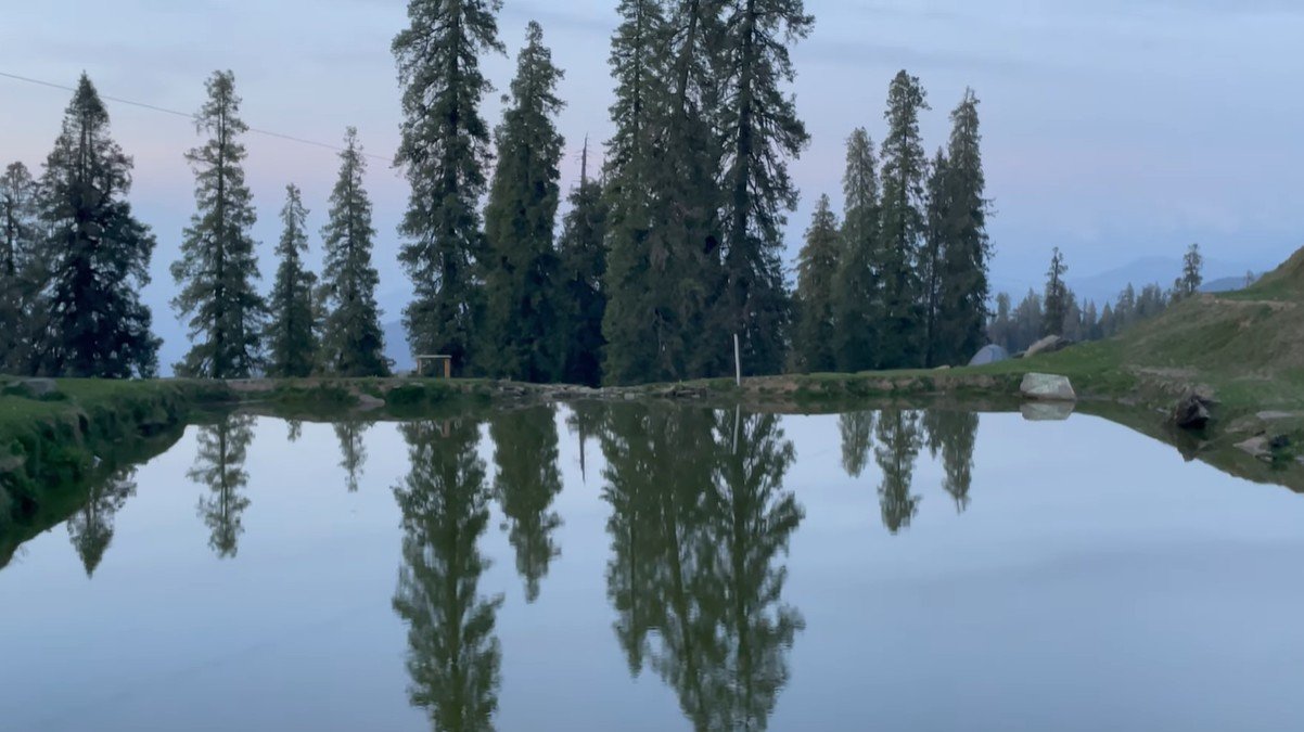 Small reflective pond surrounded by tall conifer trees below Hatu Peak