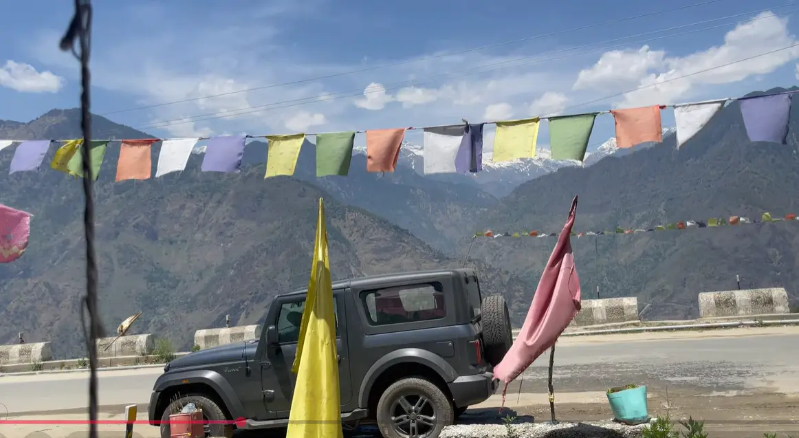 Prayer flags, parked vehicle and mountain view near Shrikhand View Dhaba in Sarahan