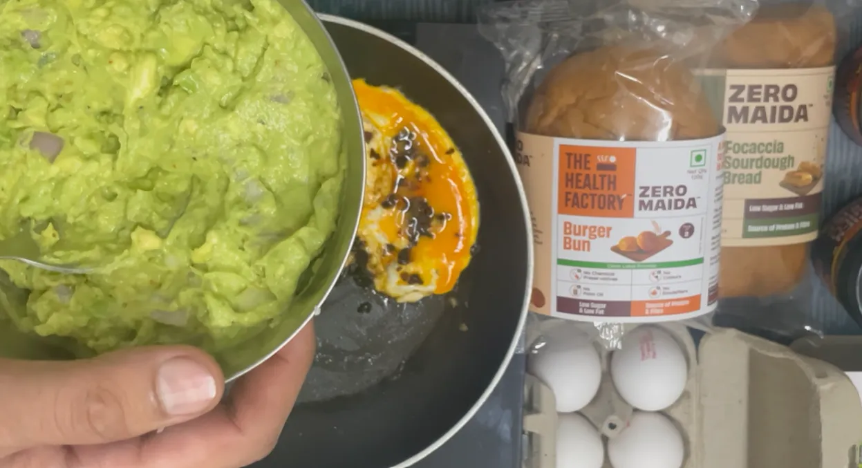 Mashed avocado and chopped onion in a bowl beside the cooking egg