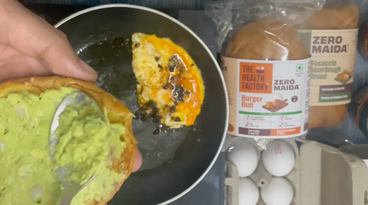Avocado and onion spread being spooned onto a toasted burger bun