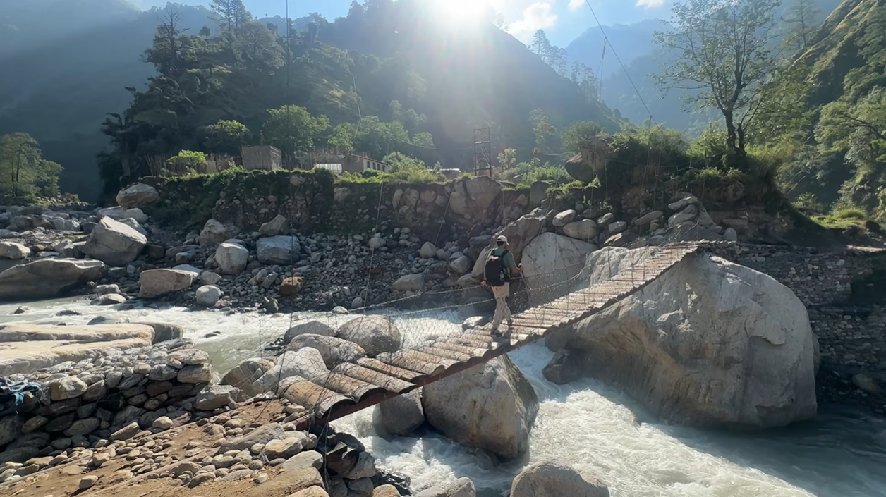 Trekker crossing a narrow suspension footbridge over the river near Bantoli