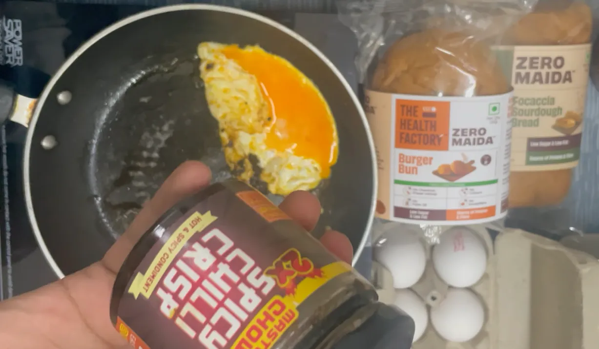 Chilli crisp jar held beside a cooking egg in the pan