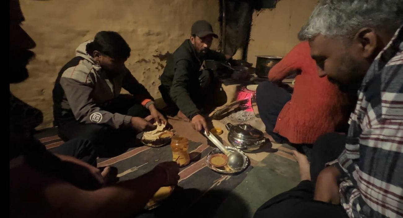 Guests eating a hot dinner beside a wood fire in a homestay kitchen