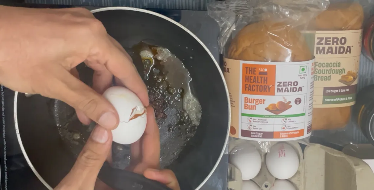 Egg being cracked over a pan with the packaged burger bun beside it