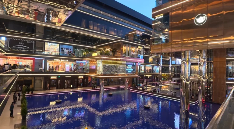 Interior view of Elan Epic Mall with illuminated shops around a large blue water feature