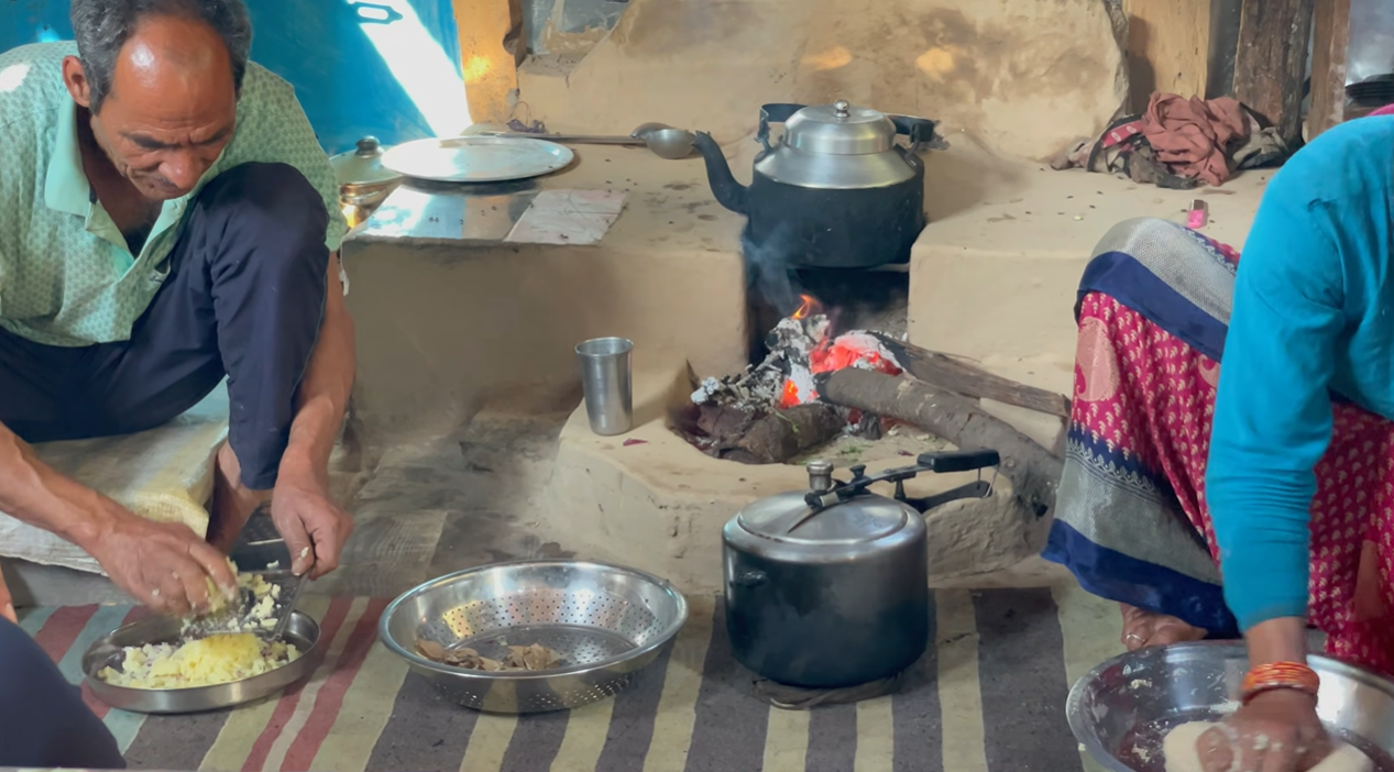 Family preparing food beside a wood-fired stove in Gaundhar