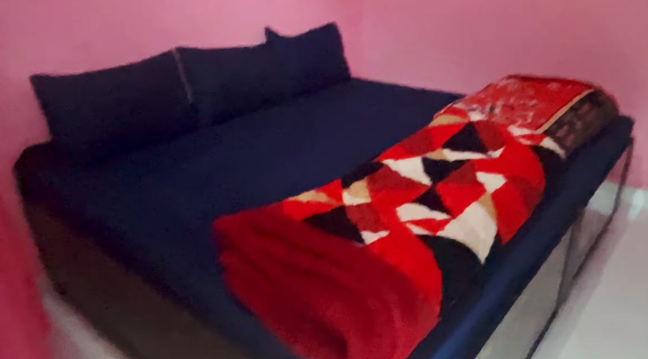 Bed with dark bedding and a red blanket in our simple Ransi hotel room