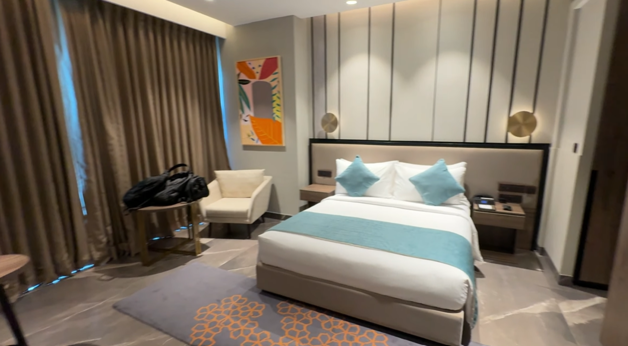 Bedroom at Citadines Paras Square Gurgaon with a teal and white bed and balcony curtains