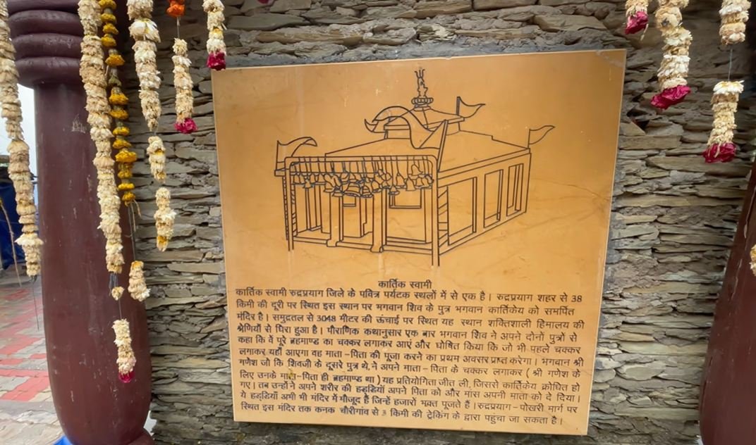 Hindi information board about Kartik Swami Temple beside a stone wall