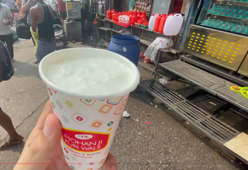 Cup of lassi with Mohan Ji Puri Wale branding held beside the street