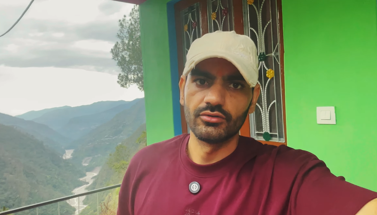 Naveen outside a green room with the river valley and hills behind him near Ransi