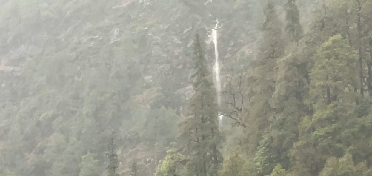 Narrow waterfall on the opposite forested hillside after rain near Chopta