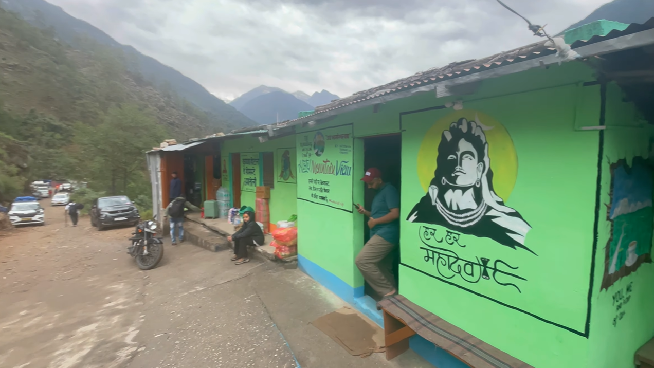 Green roadside building with a Shiva mural and parked vehicles near the Madhyamaheshwar trailhead