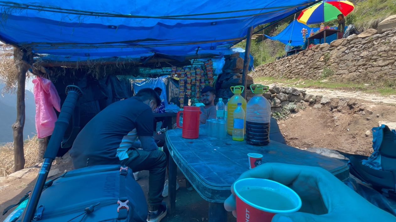 Trekking group taking a tea break under a blue tarpaulin shelter
