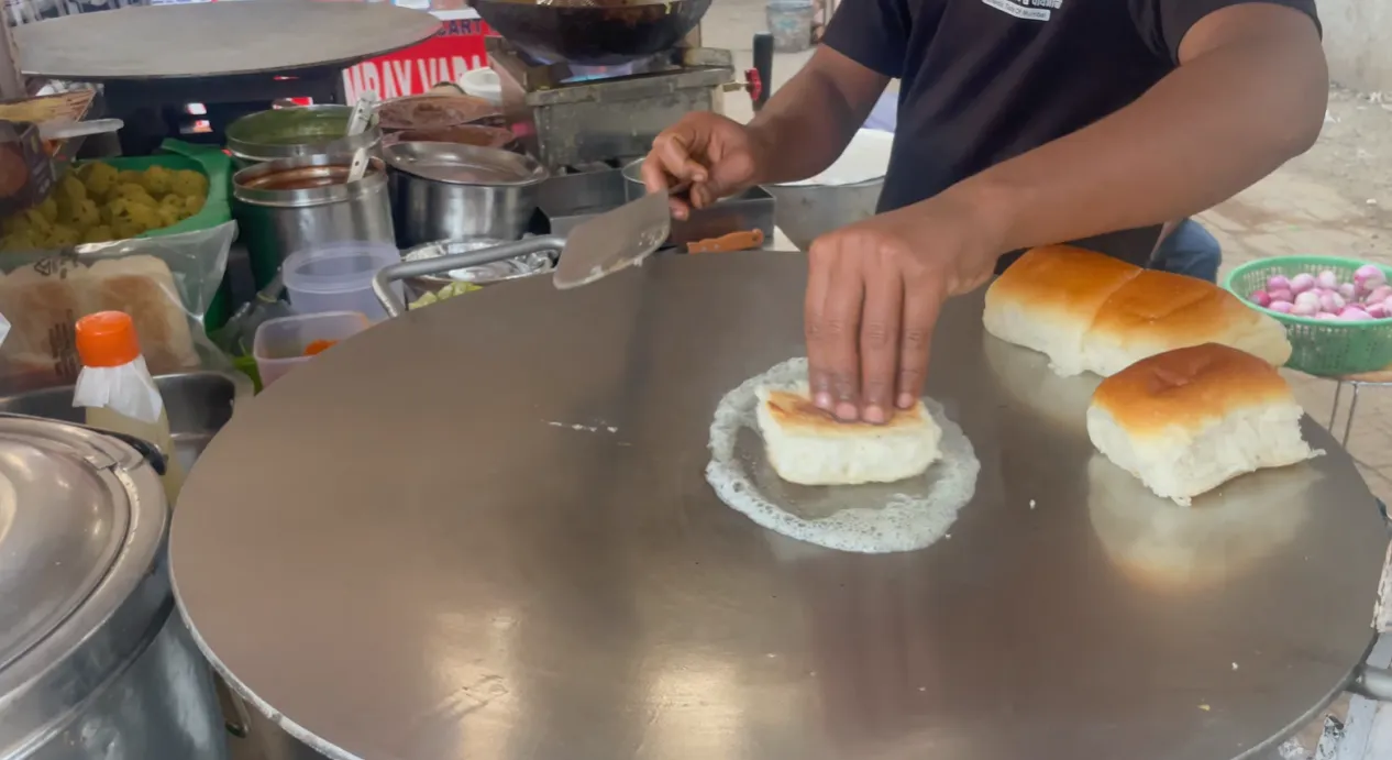 Vendor toasting pav with butter on a large tawa at the Sector 56 cart