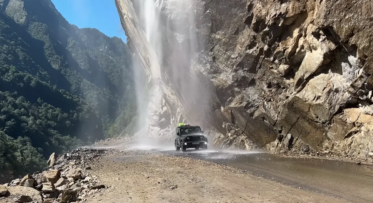 Four-wheel-drive vehicle passing beneath a large roadside waterfall